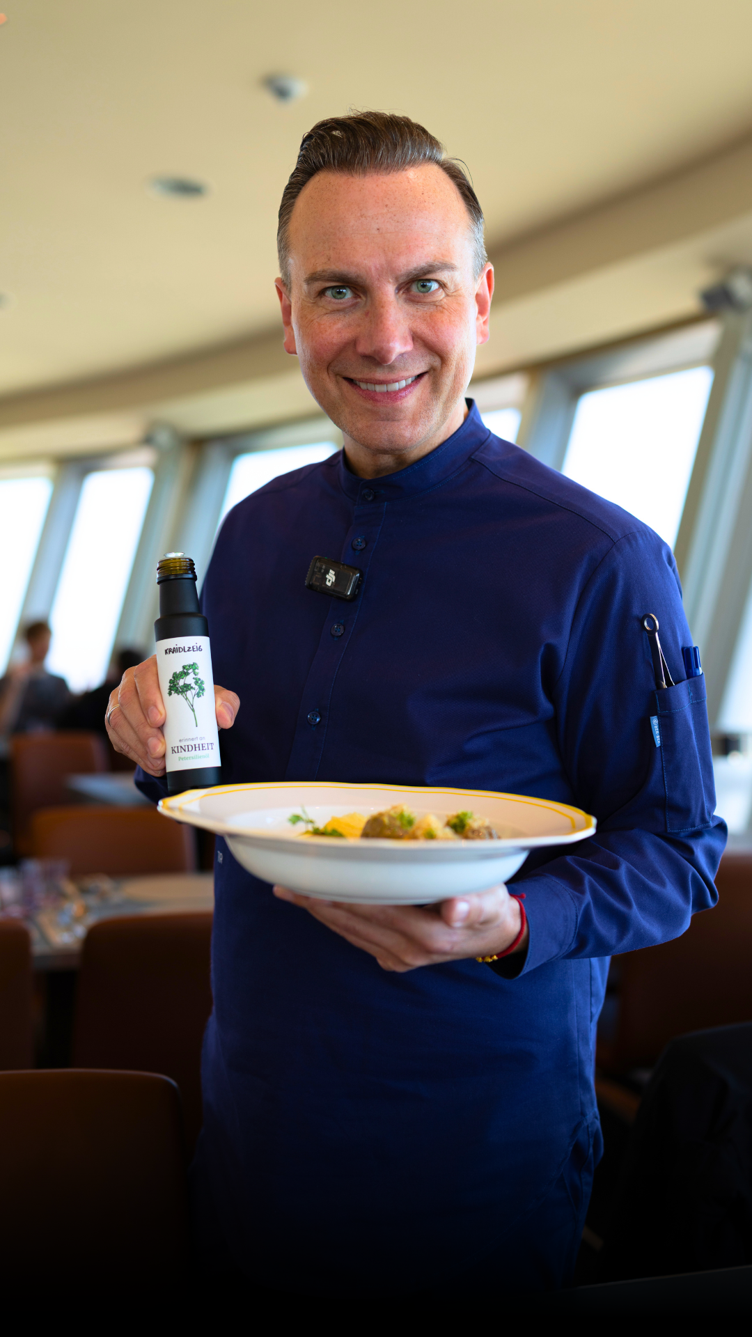 Tim Raue mit einer Flasche Kraidlzeig-Öl und einem Teller in seinem Restaurant